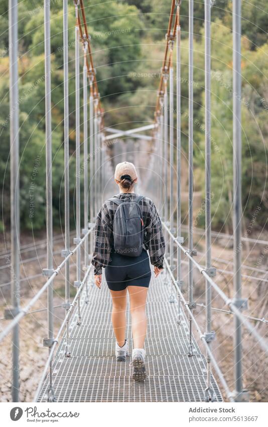 Rückenansicht einer anonymen weiblichen Wanderin in Shorts und Rucksack, die auf einem schmalen Steg läuft, während sie während eines Wochenendausflugs im Wald wandert