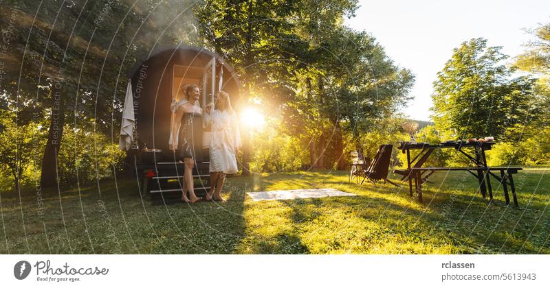 Zwei Personen, die bei Sonnenaufgang ein finnisches Saunafass in einem Wald mit einem Picknicktisch in der Nähe verlassen. Tisch Frau glückliche Menschen