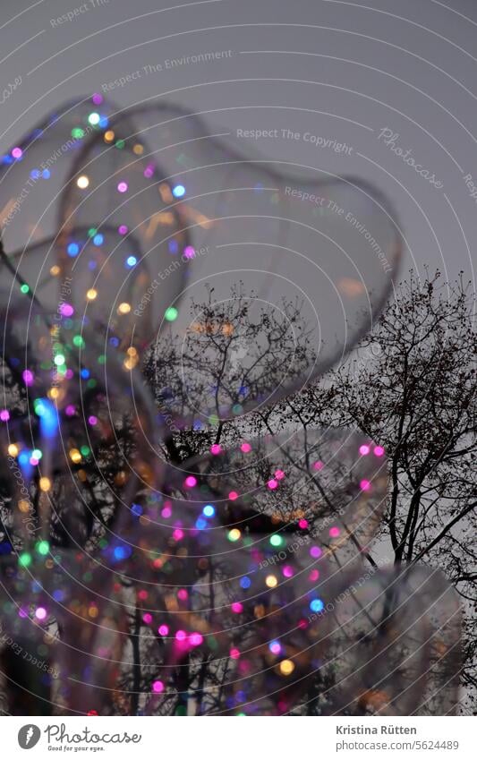 bunte lämpchen in herzballons und trüber winterhimmel lichter luftballons duchsichtig leds leuchten dämmerung abends draußen bäume dunkel