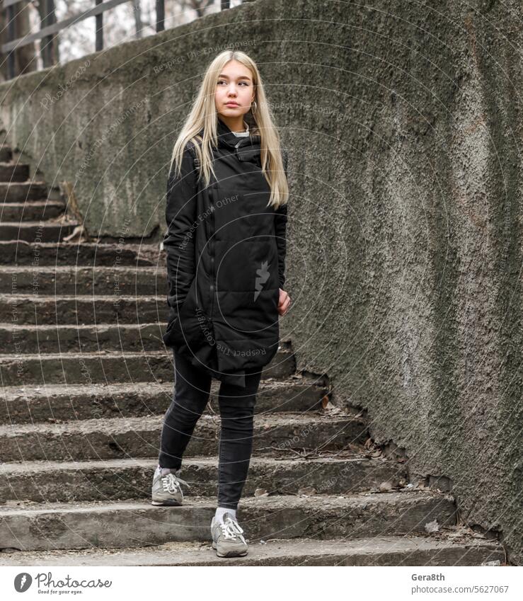 Ein junges Mädchen mit blonden Haaren in schwarzer Kleidung kommt die Steintreppe herunter. Erwachsener Herbst schwarze Kleidung blondes Haar Großstadt