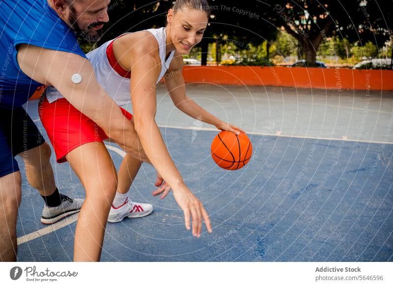 Entschlossener Mann und Frau in Sportkleidung spielen Basketball auf einem Spielplatz in einer Stadt mit Gebäuden und Bäumen im Hintergrund Sportler Ball wehren