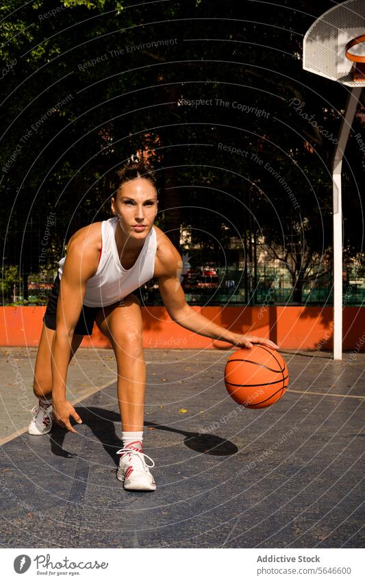 Ganzer Körper einer sportlichen jungen Frau in Sportkleidung, die wegschaut, während sie an einem sonnigen Sommertag auf dem Platz Basketball spielt Sportlerin