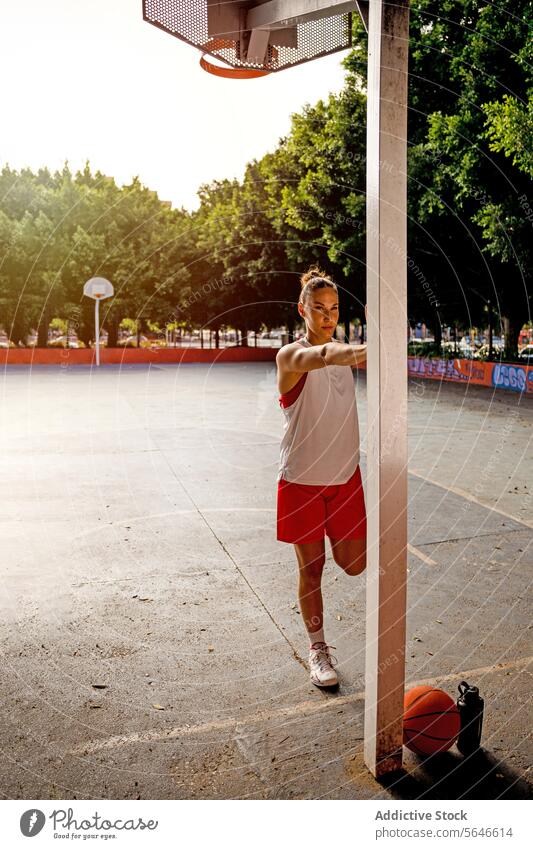 Selbstbewusste, fitte Frau in Sportkleidung steht in der Nähe des Pfostens und macht Aufwärmübungen, bevor sie auf dem Platz Basketball spielt Sportlerin