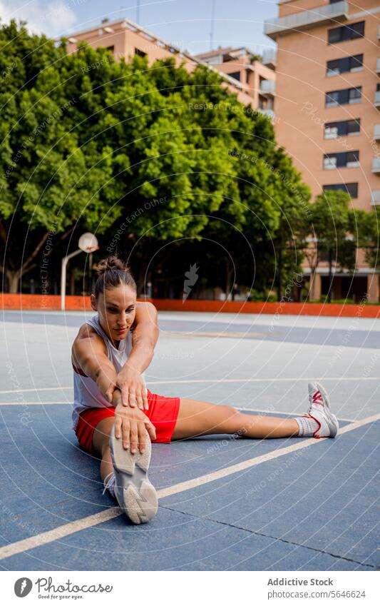 Ganzer Körper einer entschlossenen jungen Basketballspielerin, die sitzt und die Füße berührt, während sie auf dem Spielplatz Aufwärmübungen macht Sportlerin