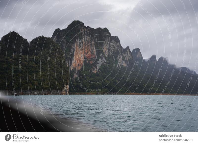 Boot schwimmt auf einem kräuselnden See in der Nähe hoher Berge in Thailand Menschen Tourist reisen Berge u. Gebirge felsig Natur Cloud Grün Cheow Lan See Asien