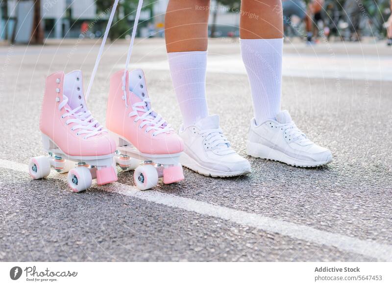 Crop-Frau in trendigen Turnschuhen steht neben rosa Quad-Skates auf der Straße Skateboard Teenager Bein Schlittschuh Großstadt Schuhe Kniestrümpfe Stil jung