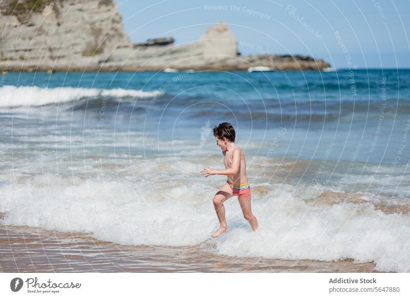 Kleiner Junge genießt spielerischen Lauf am sonnigen Strand laufen spielen winken Ufer Sand MEER Meer Sommer Spaß Kind im Freien Küste malerisch Natur Urlaub