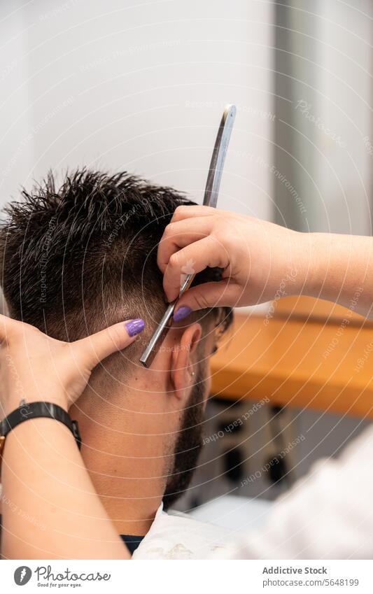 Abgeschnittene, nicht erkennbare Hände einer Friseurin, die das Haar eines männlichen Kunden mit einem Rasiermesser im Salon stylt Gerades Rasiermesser Mann