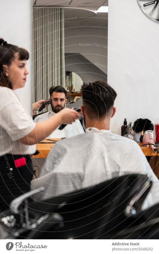 Seitenansicht einer fokussierten Friseurin, die einen elektrischen Trimmer an den Haaren eines männlichen Kunden im Salon benutzt Mann Behaarung Pflege Dienst