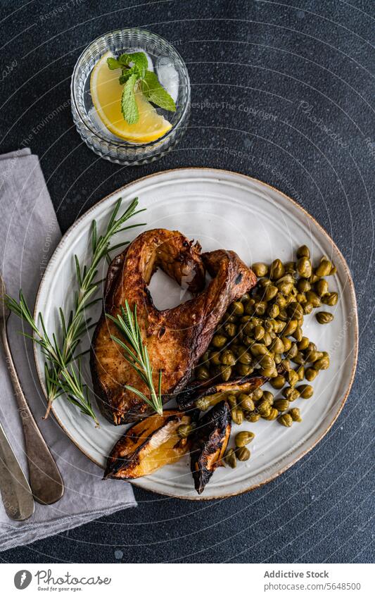 Gegrilltes, gewürztes Lachssteak mit fermentierten Kapern, verkohlter Zitrone und einem Zweig Rosmarin, dazu ein erfrischendes Zitronenwasser grillen Steak