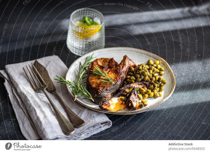 Von oben gegrilltes Lachssteak mit fermentierten Kapern und einer Zitronenspalte, garniert mit frischem Rosmarin auf einem rustikalen Keramikteller mit Vintage-Besteck