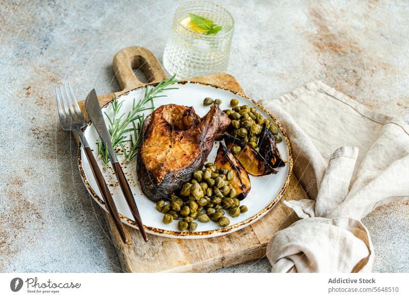 Ein gesundes, gegrilltes und gewürztes Lachssteak mit gerösteten Zitronen und Kapern auf einem Holzbrett mit einer Leinenserviette und Zitronenwasser Gesundheit