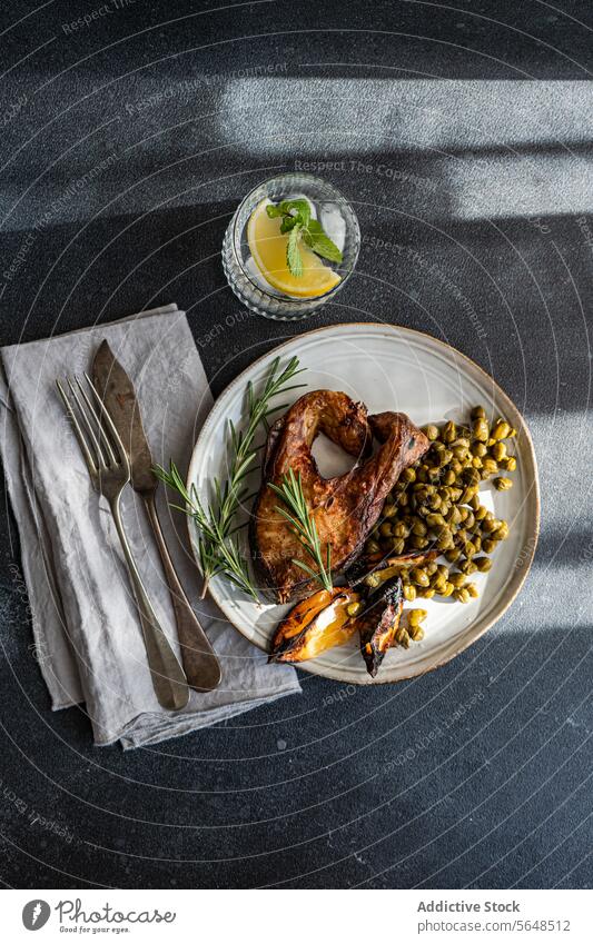 Gegrilltes, gewürztes Lachssteak mit fermentierten Kapern, verkohlter Zitrone und einem Zweig Rosmarin, dazu ein erfrischendes Zitronenwasser grillen Steak