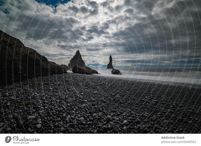 Zerklüftete Felsen ragen aus dem nebligen Meer vor dem Kiesstrand eines dramatischen isländischen Strandes unter einem wolkenverhangenen Himmel Island MEER