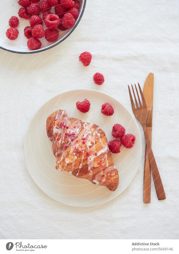 Leckeres Croissant mit Himbeere auf Teller und Besteck auf Marmoroberfläche im Restaurant Himbeeren lecker Lebensmittel appetitlich Speise Dessert geschmackvoll