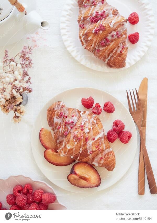 Draufsicht auf ein Frühstück mit Croissants und Obst auf einem weißen Tisch neben Teekanne und Besteck Frucht Tischwäsche golden Zuckerguß farbenfroh Streusel