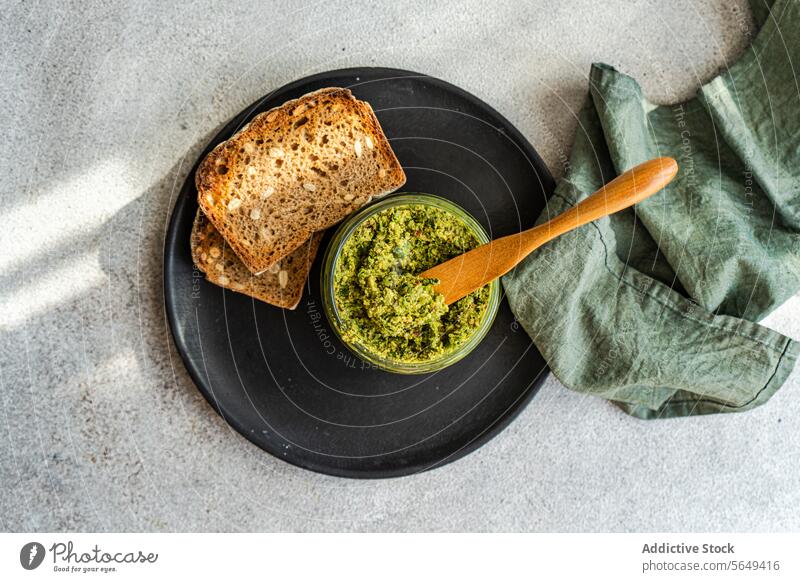 Leckeres Roggenbrot mit Pestoaufstrich, serviert mit Löffel und Serviette Saucen Teller geschmackvoll selbstgemacht lecker Brot Schalen & Schüsseln Besteck