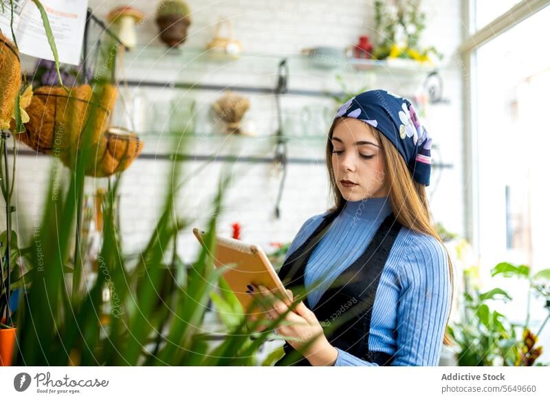 Floristin bei der Arbeit im Blumenladen mit Tablet Frau Blumenhändler benutzend Tablette Bestandsaufnahme Checkliste Management eingetopft Pflanze jung Schürze