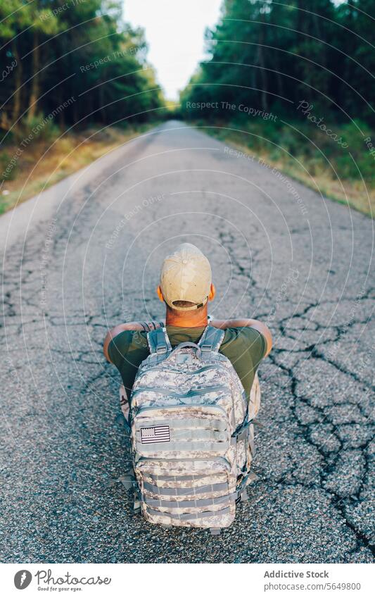 Rückenansicht von Anonymous mittleren Alters Armee Kommando mit Rucksack sitzen auf der Straße gegen Wald Mann Soldat Militär anonym Tarnung Verschlussdeckel