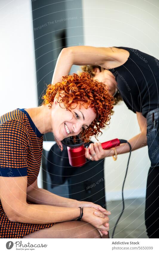 Friseur, der das lockige Haar einer Frau mit einem Haartrockner stylt stylen krause Haare rote Haare Salon Lächeln modern Schönheit Mode Frisur Pflege