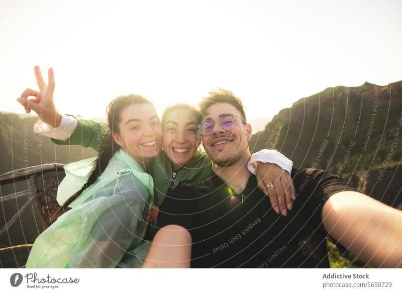 Porträt von fröhlichen kaukasischen aktiven jungen Freunden, die ein Selfie machen und dabei in die Kamera schauen, auf einem Berggipfel während des Sonnenaufgangs beim Wandern am Wochenende