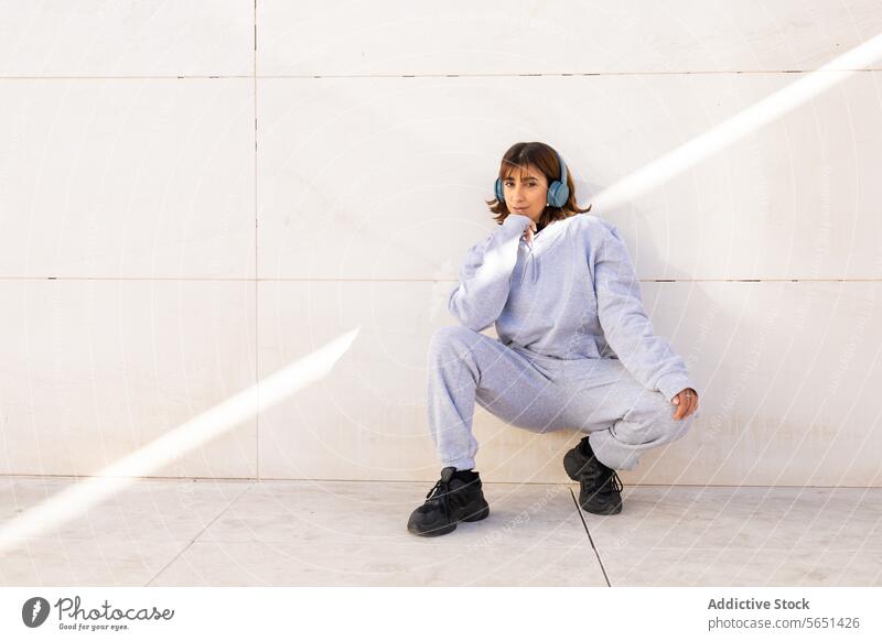 Junge Frau in Freizeitkleidung mit Kopfhörern beim Entspannen jung entspannend lässig Kleidung Musik Trainingsanzug blau Turnschuh minimalistisch Hintergrund