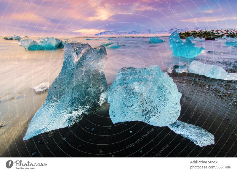 Eisberge am schwarzen Sandstrand mit einem bunten Sonnenaufgang und schneebedeckten Bergen im Hintergrund in Island schwarzer Sandstrand Berge u. Gebirge Schnee