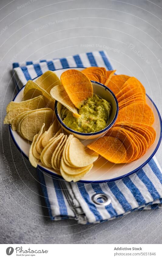 Gemischte Chips mit Guacamole im Betonhintergrund Kartoffelchips Paprika Käse Avocado Saucen Snack Teller Schalen & Schüsseln gestreift Serviette Amuse-Gueule