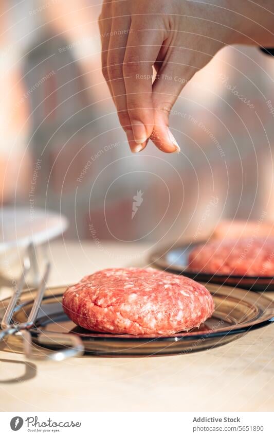 Würzen eines Pattys für gegrillte Burger Hand Gewürz Salz Berieselung Pastetchen roh Vorbereiten Grillen Nahaufnahme Fleisch Essen zubereiten Vorbereitung