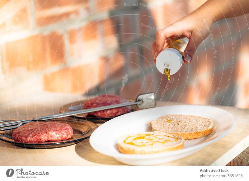 Burger-Patties und Brötchen zum Grillen vorbereiten Pastetchen Olivenöl Hand eingießen roh Zubereitung von Speisen Barbecue Essen zubereiten im Freien