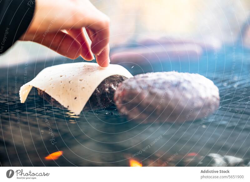 Schmelzender Käse auf einem Burger beim Grillen im Freien Hand Scheibe Pastetchen Grillrost Flamme Barbecue Essen zubereiten Zubereitung von Speisen