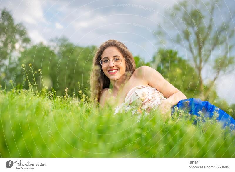 glückliche junge Frau mit Brille liegt auf einer Wiese frau lachen hübsch single fröhlich porträt attraktiv optimistisch entspannt freude selbstbewusst