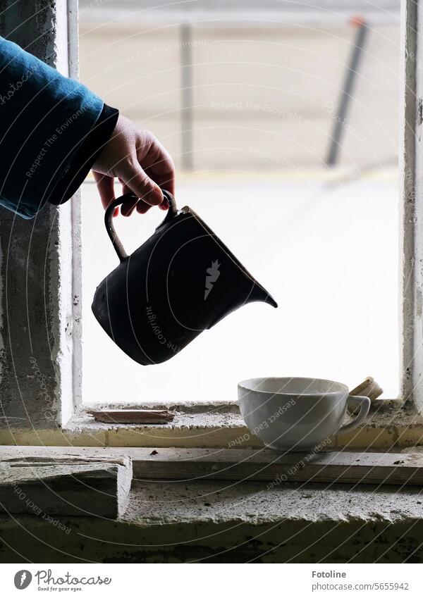 Die Hand hält ein altes Kännchen und tut so, als würde sie etwas in die Tasse gießen. Kanne weiß Porzellan Geschirr Keramik schwarz Fensterrahmen Finger Ärmel