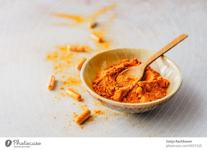 Kurkuma Pulver in einer Schüssel mit einem Holzlöffel und Kapseln auf einem grauen Tisch. Nahaufnahme Löffel Lebensmittel Gewürz Gesundheit aromatisch Medizin