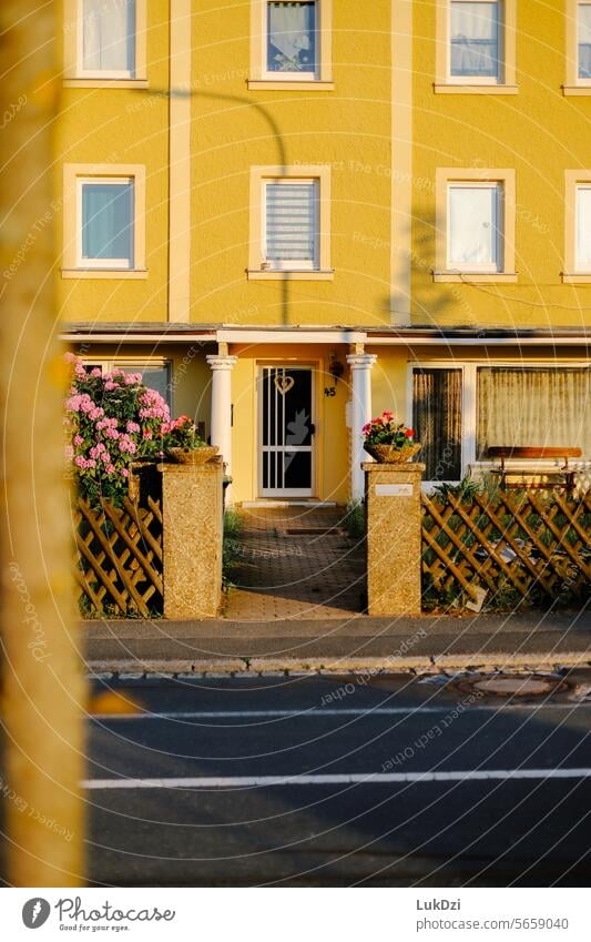 die Fassade und der Eingang eines gelben zweistöckigen Hauses, das von den Strahlen der aufgehenden Sonne beleuchtet wird, ohne Menschen schließen braun