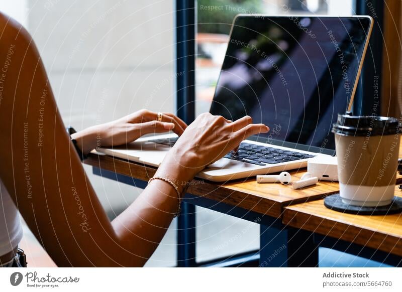 Abgeschnittene, nicht erkennbare Frauenhände, die auf einem Laptop tippen, mit einer Kaffeetasse und einem Smartphone auf dem Tisch, konzentriert während einer Fernarbeitssituation in Chiang Mai, Thailand