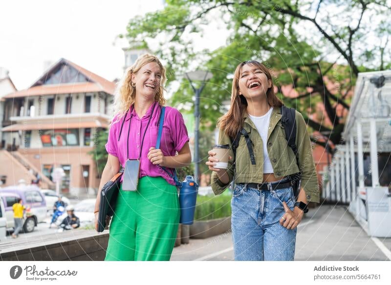 Fröhliche multiethnische Frauen gehen im Freien spazieren, eine von ihnen hält eine Kaffeetasse, in einer entspannten Umgebung nach der Arbeit in Chiang Mai, Thailand