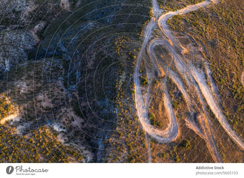 Das Licht des Sonnenuntergangs wirft Schatten auf eine gewundene Schotterstraße, die sich durch die hügelige Landschaft von Alcarria schlängelt Antenne