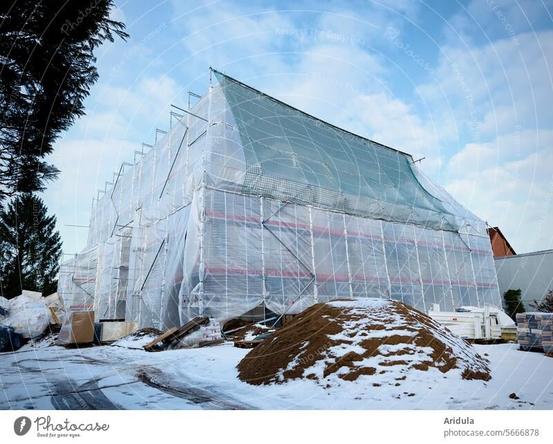 Eingehülltes Haus auf einer Baustelle im Winter Baugerüst Bauplane Baunetz Baufolie Netz Renovierung Gerüst Abdeckung Fassade Gebäude Sanieren Renovieren