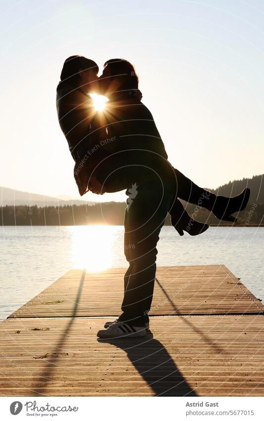 Ein Paar küsst sich bei Sonnenuntergang auf einem Steg am Wasser Mann Frau paar küssen kuss liebe Liebesbeweis sonnenuntergang Sonnenschein Brücke Sommer