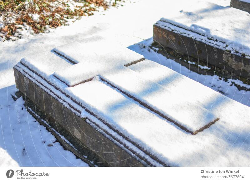 eine verschneite alte steinerne Grabplatte mit Kreuz Friedhof Schnee Grabstein Grabstätte Grab verschneit Tod Trauer Vergänglichkeit Grabmal ruhig Stein