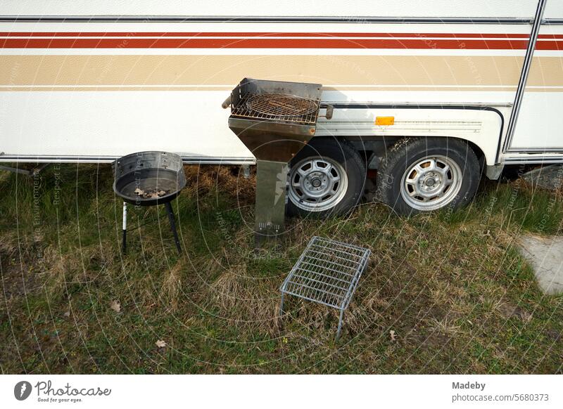 Campinggrill und Holzkohlengrill vor einem Wohnwagen mit Tandembereifung für Vanlife und Camping auf dem Campingplatz am Segelflugplatz Oerlinghausen bei Bielefeld im Teutoburger Wald in Ostwestfalen