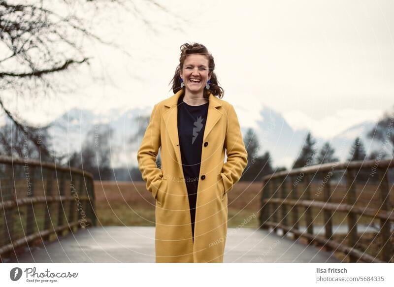 FREUDIG - WARTEN - BERGLANDSCHAFT Frau 30 bis 40 Jahre Locken blond gelb Mantel Berge u. Gebirge Brücke Holz warten freudig lachen Lebensfreude Zufriedenheit