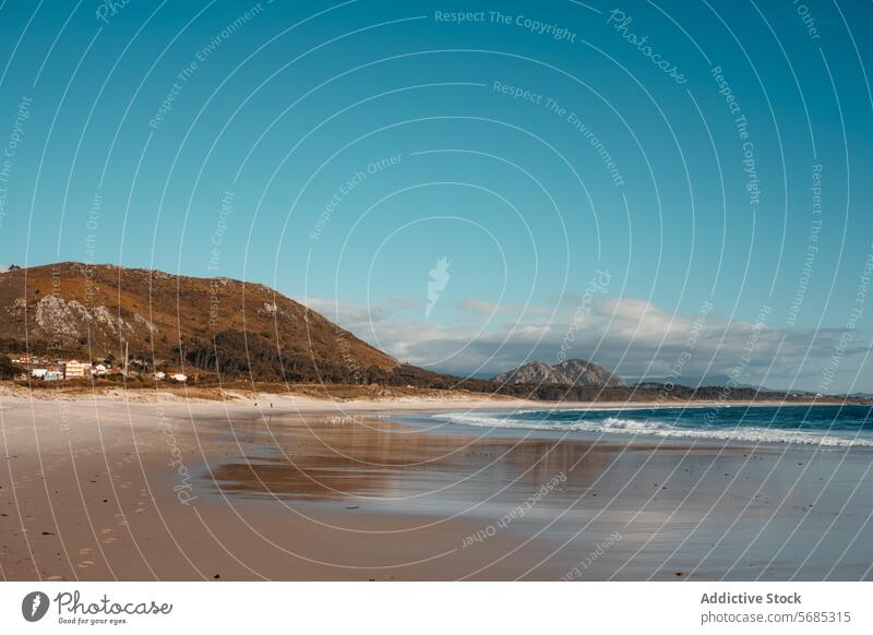 Der weitläufige Strand von Lariño in Galicien mit seinem feinen Sand, den sanften Wellen und den zerklüfteten Hügeln im Hintergrund unter einem klaren Himmel