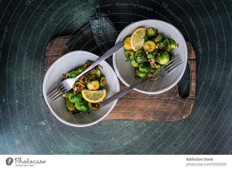 Schüssel mit gegrilltem Rosenkohl, gewürzt mit Knoblauch und Gewürzen, garniert mit einer Zitronenscheibe, serviert auf einem Holzbrett mit einer Gabel