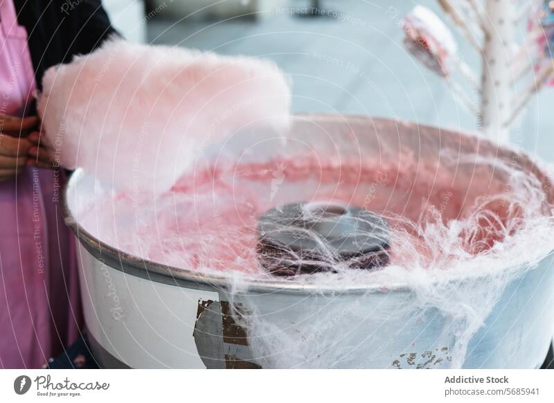 Eine abgeschnittene, nicht erkennbare Person, die auf einem Jahrmarkt mit einer Spinnmaschine eine große, flauschige Zuckerwatte herstellt Baumwolle Bonbon