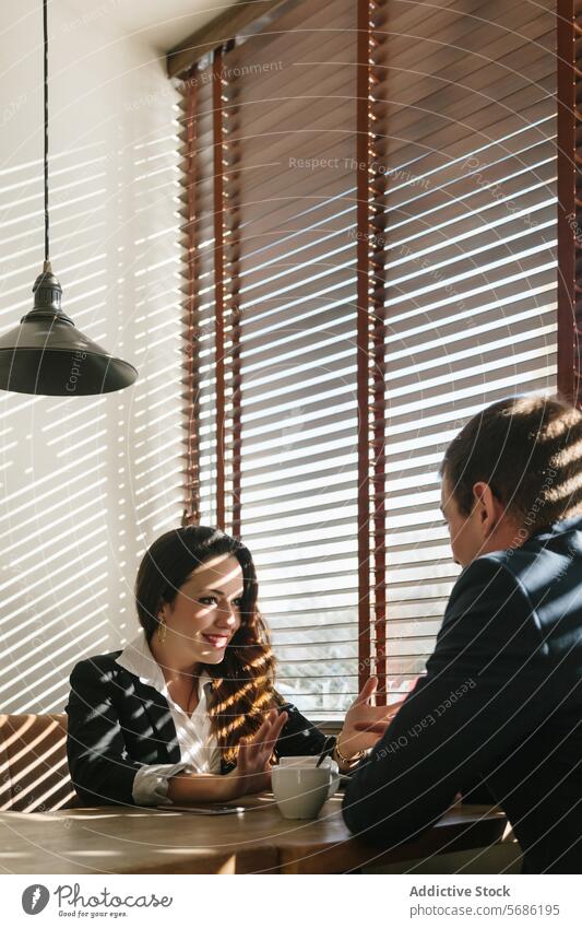 Geschäftstreffen in einem Madrider Café mit Sonnenlichtmustern Sitzung professionell Business Frau Mann Kaffee Gespräch Besprechung Anzug Jalousien Licht