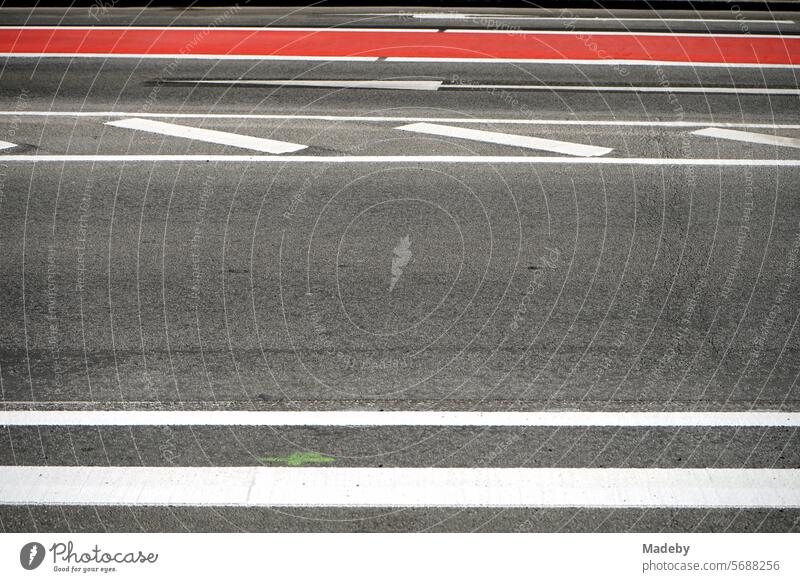 Weiße Fahrbahnmarkierung auf grauem Asphalt und rote Markierung für den Radweg bei Sonnenschein in der Berliner Straße in Frankfurt am Main in Hessen asphalt