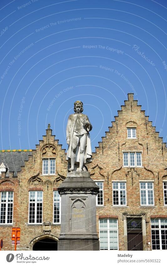 Statue von Hans Memling am Woensdagmarkt mit schönem alten Treppengiebel aus Backstein vor blauem Himmel im Sonnenschein in den Gassen der Altstadt von Brügge in Westflandern in Belgien