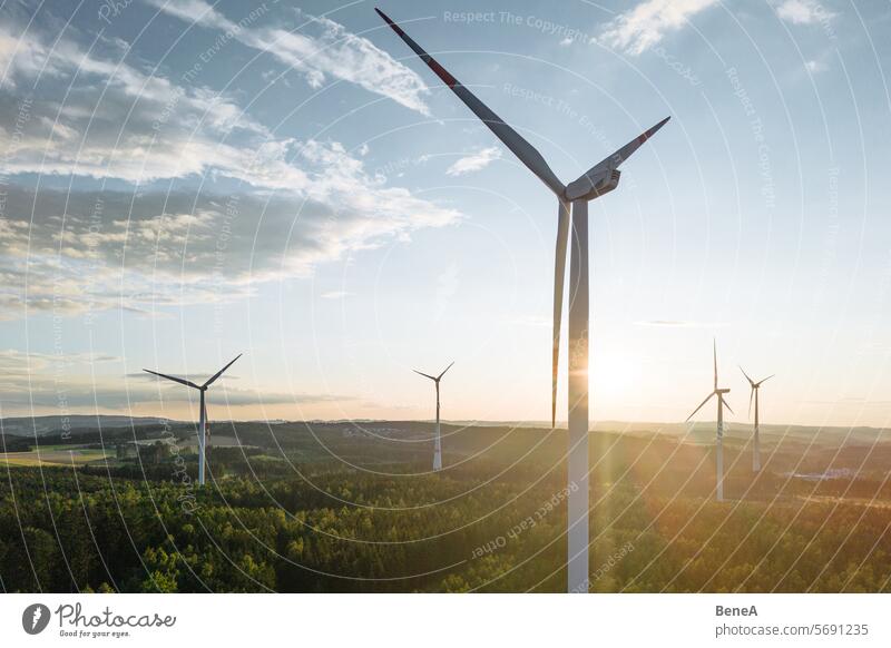 Windkraftanlagen in einem hügeligen Wald vor einem teilweise bewölkten, aber sonnigen Himmel aus der Vogelperspektive bei Sonnenuntergang Antenne Sauberkeit